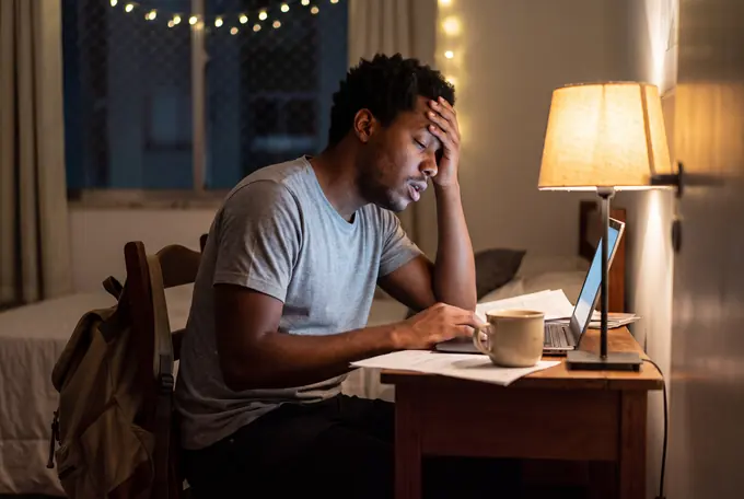 Estudante cansado diante do notebook, tarde da noite